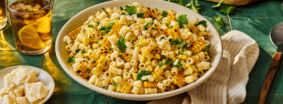Shot of white bowl with Mexican-inspired corn pasta salad with ditali pasta and topped with cilantro and feta cheese