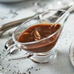 Glass gravy boat filled with brown gravy and onions