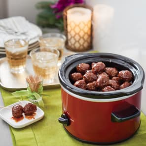 Slow cooker filled with glazed meatballs on a table with drinks